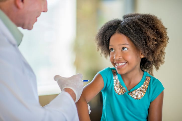 A child smiles as a provider administers a vaccine