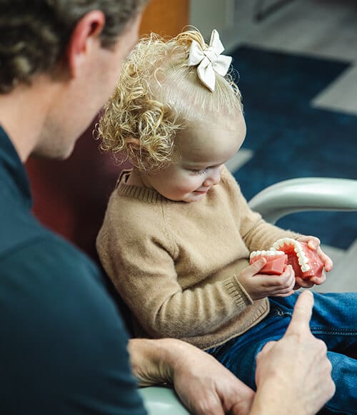 A young patient holds a model of teeth