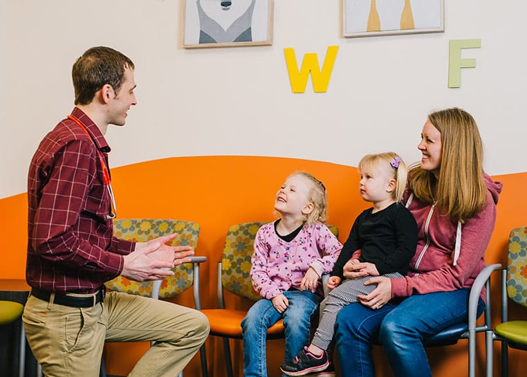 Parent and children smile at a pediatrician in a clinical setting