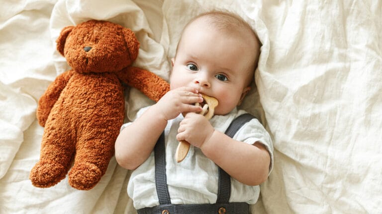 Baby with teddy bear chewing on a teething toy