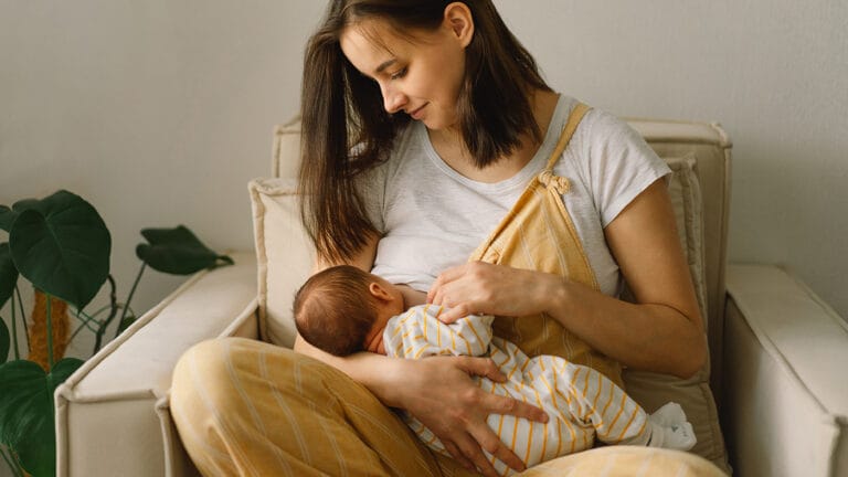 young mom sitting on the couch breast feeding her new baby