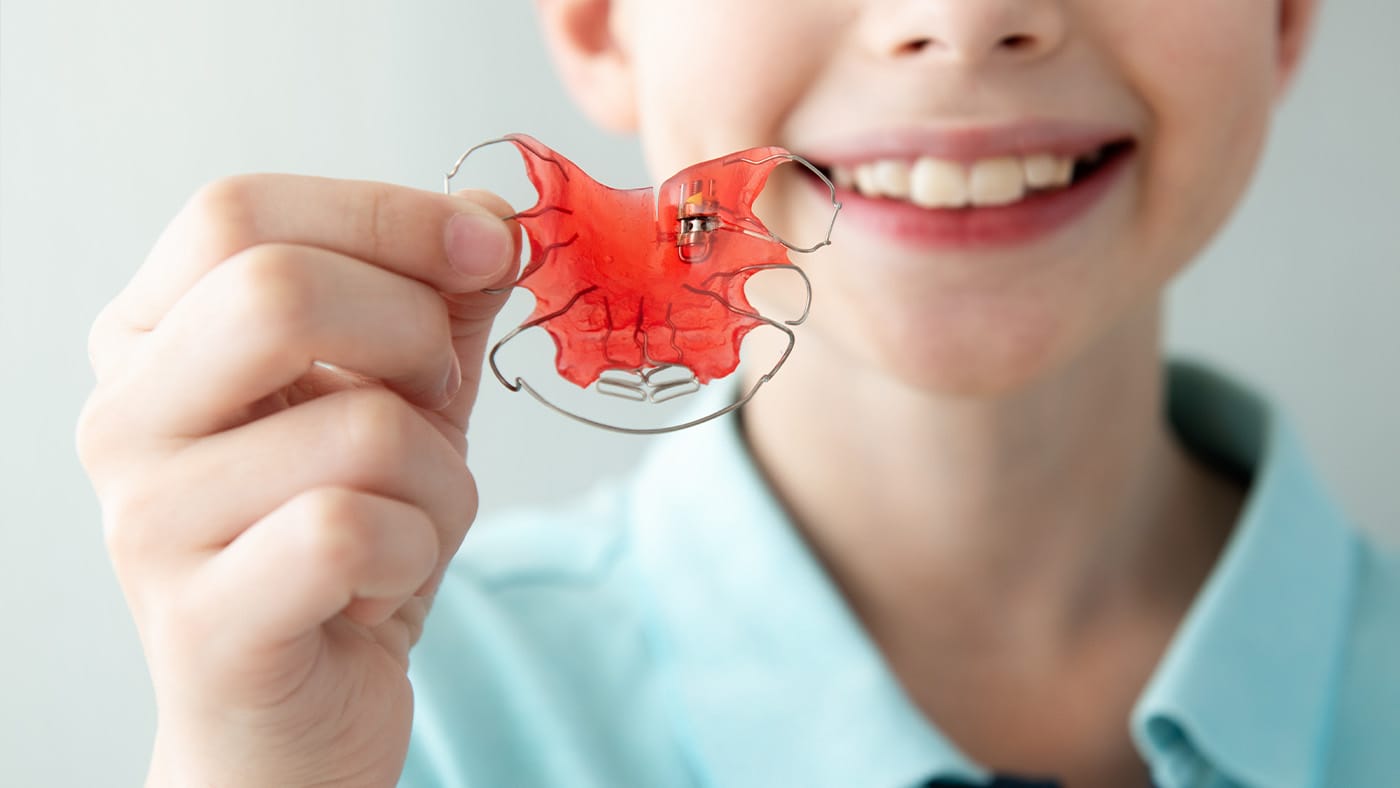 Young boy holding up retainer