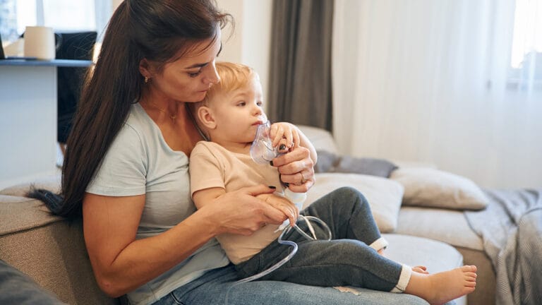 mom holding toddler while giving him a breathing treatment