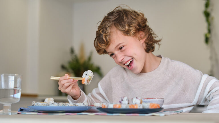 Young boy with braces eating sushi with chopsticks