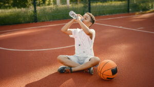 Young boy on basketball court drinking water from bottle