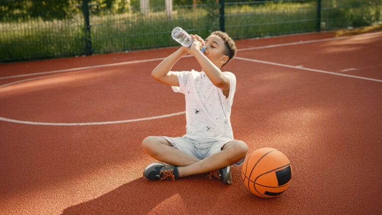 Young boy on basketball court drinking water from bottle