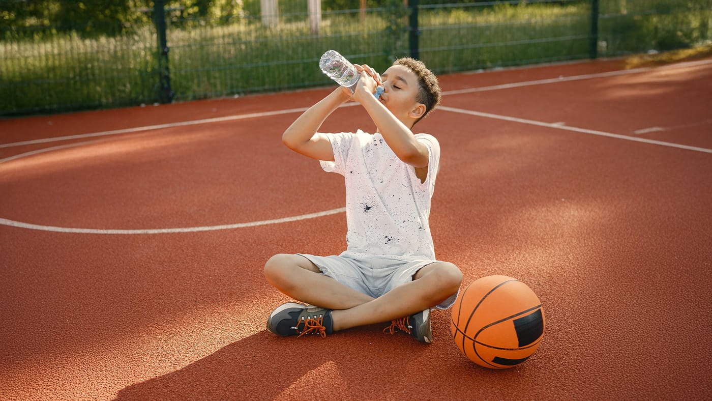 Young boy on basketball court drinking water from bottle