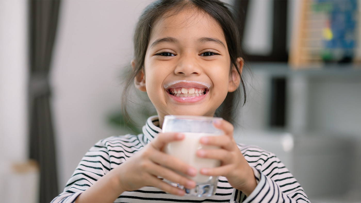 Little girl with a glass of milk smiling with a milk mustache