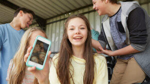 Group of tweens hanging out together, while the girl in the middle shows the camera a selfie of the group