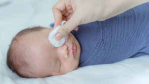 A newborn sleeping while his mother cleans his eye with a cotton pad