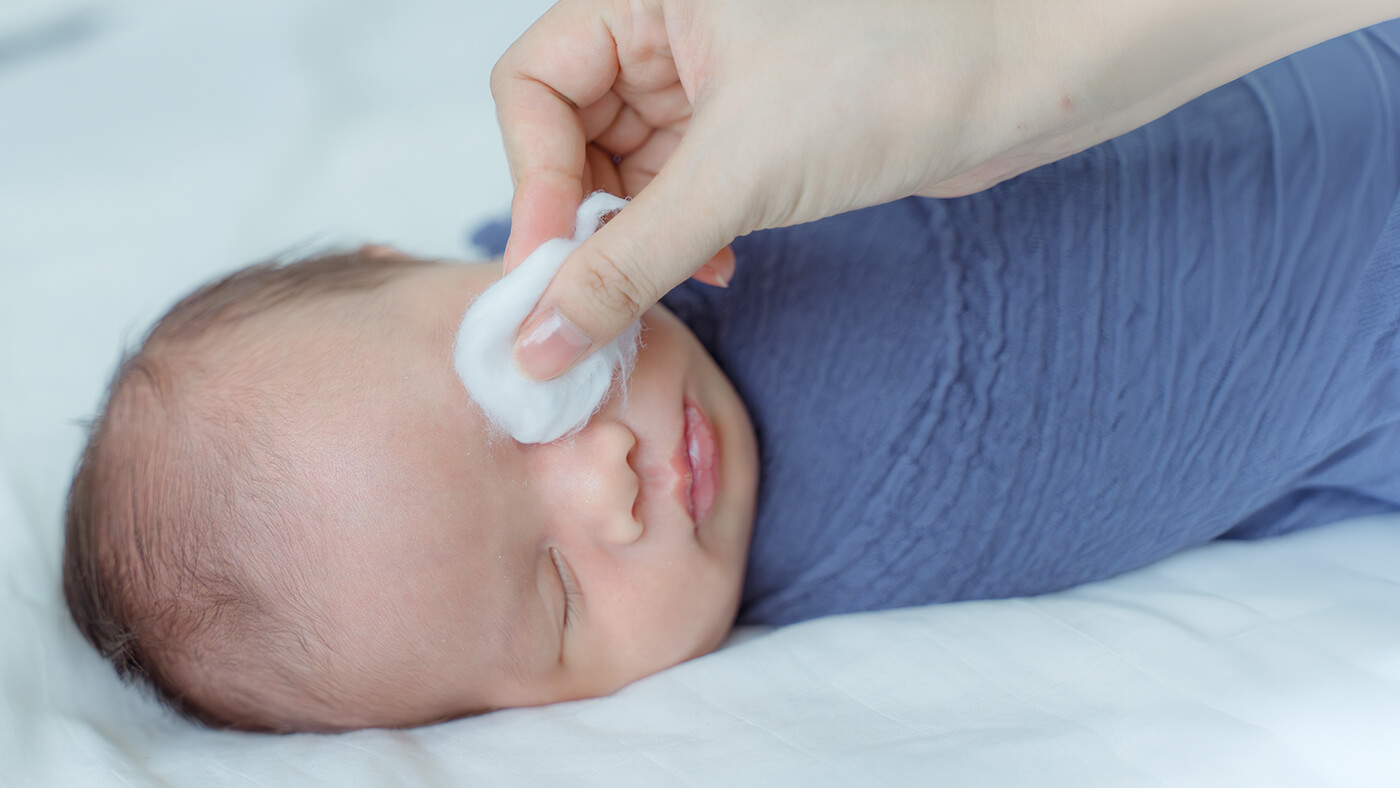 A newborn sleeping while his mother cleans his eye with a cotton pad