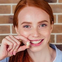 Teen smiling while holding their extracted wisdom tooth