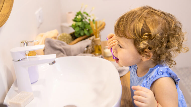 young toddler brushing her teeth in the mirror