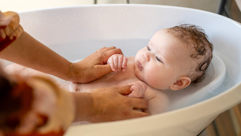Parent washing their newborn in a small tub